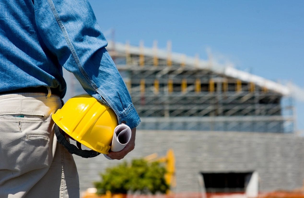 A construction worker holding his helmet in the air.